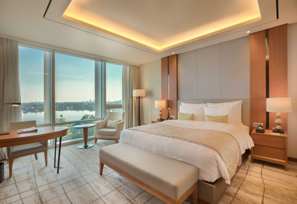 a luxurious hotel room with a large bed , a dresser , and a window overlooking the ocean at Lotte Hotel Yangon