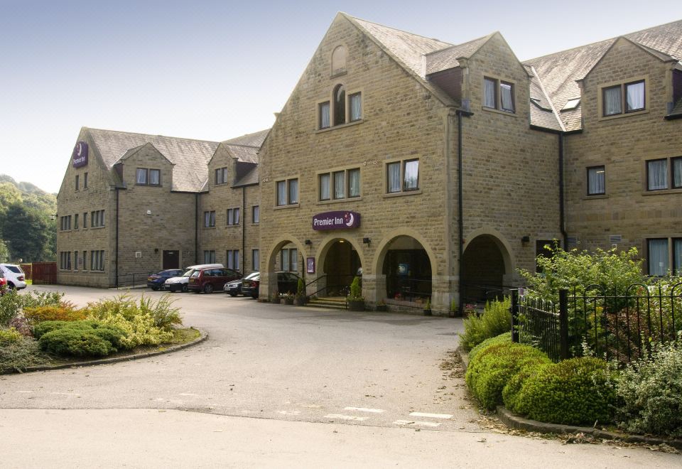 a large stone building with a purple sign on the front , surrounded by trees and cars at Huddersfield North
