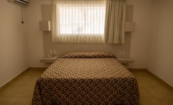 a bed with a floral patterned blanket is positioned in front of a window with white curtains at Hotel St. George