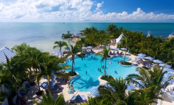 a large outdoor pool surrounded by palm trees and other tropical plants , with people enjoying their time in the water at Isla Bella Beach Resort & Spa - Florida Keys
