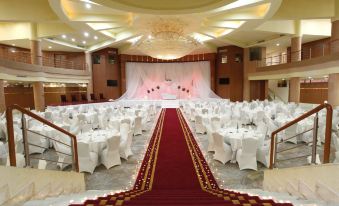 a large banquet hall with white tables and chairs , red and gold decorations , and a stage at Tunis Grand Hotel