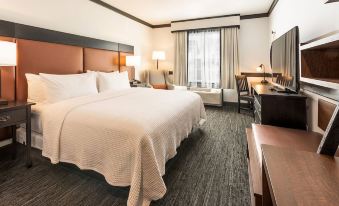 a large bed with white sheets and pillows is in a room with a desk , chair , and window at The Craftsman Inn & Suites