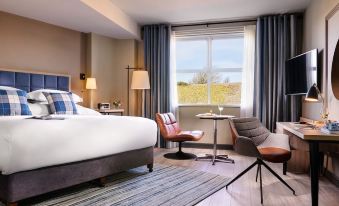 a modern hotel room with a large bed , two chairs , and a window overlooking the outdoors at Harbour Hotel
