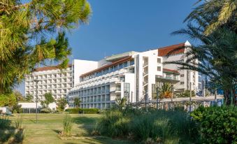 a large white building surrounded by trees , with a grassy field in front of it at Grand Hotel Ontur Cesme