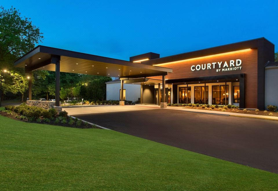 "a modern hotel entrance with the name "" courtyard by marriott "" prominently displayed , surrounded by lush green grass and trees" at Courtyard Lincroft Red Bank