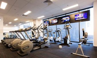 a gym with various exercise equipment , including treadmills and stationary bikes , is shown in front of large windows at The Larwill Studio Melbourne - Art Series