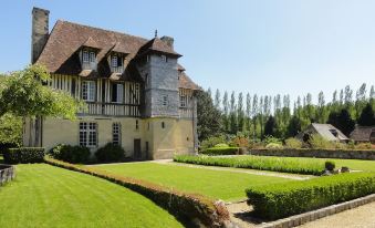 a large stone house surrounded by a lush green lawn , with trees in the background at Les Manoirs des Portes de Deauville - Small Luxury Hotel of the World