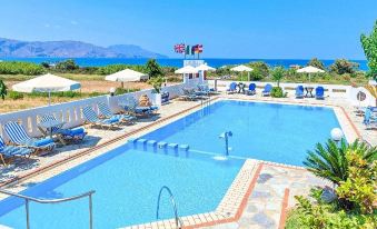 a large outdoor swimming pool surrounded by lounge chairs and umbrellas , with a view of the ocean in the background at Palladion