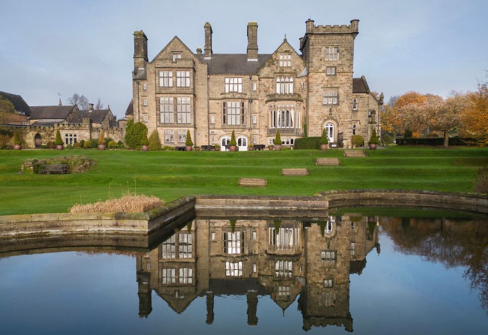 a large stone mansion surrounded by grass and trees , with a pond in the background at Delta Hotels Breadsall Priory Country Club
