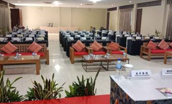 a large , empty banquet hall with rows of tables and chairs , as well as potted plants and bottles of water at Hotel Grand Papua Kaimana