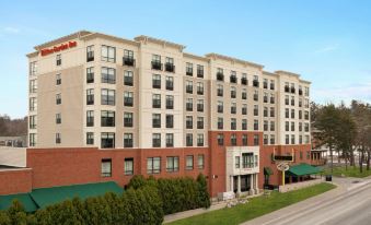 a large hotel building with a red sign on the front , situated in a city setting at Hilton Garden Inn Troy