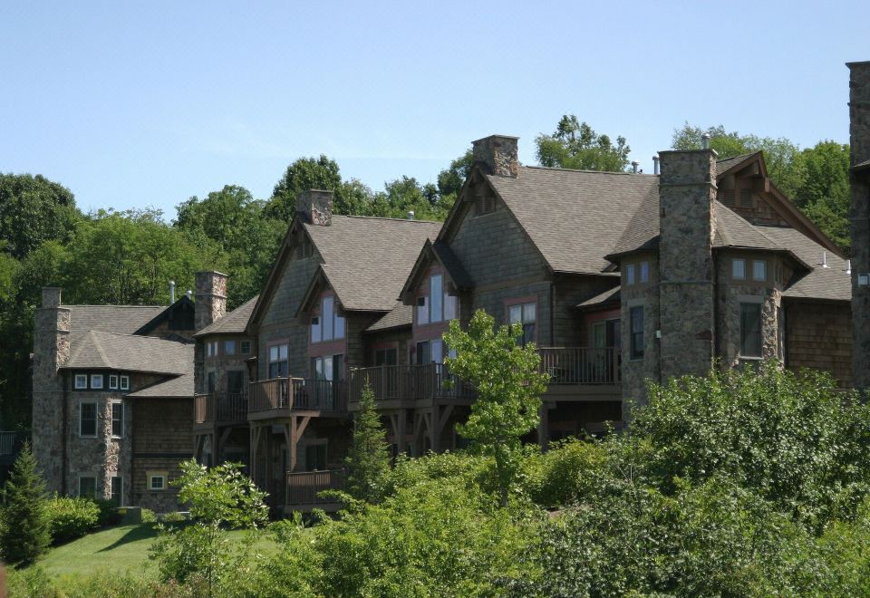 a large wooden house with multiple balconies and windows , surrounded by lush green trees and a clear blue sky at The Appalachian at Mountain Creek