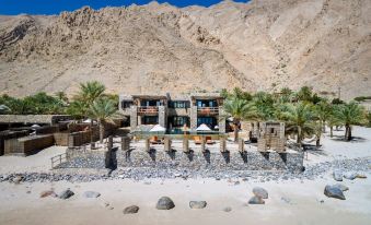 a large building is surrounded by rocks and palm trees in front of a mountain at Six Senses Zighy Bay