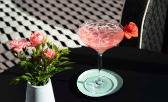 a cocktail glass with a strawberry garnish is placed on a table next to a vase of flowers at Best Western Plus Hotel les Rives du Ter