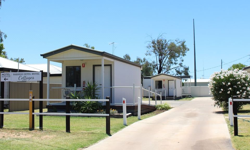 a row of small , white mobile homes with green grass and trees in front of them at Warrego Hotel Motel Cunnamulla