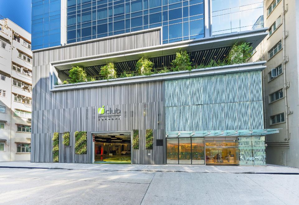The front entrance of a large building features an outdoor seating area and glass facade on both sides at iclub To Kwa Wan Hotel