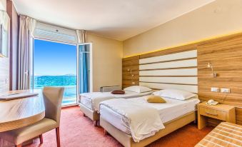 a hotel room with two beds , a chair , and a window overlooking the ocean , creating a serene atmosphere at Hotel Panorama