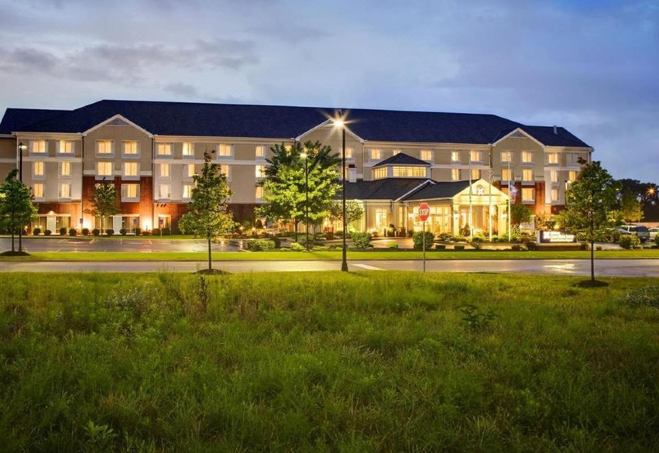 a large hotel building lit up at night , surrounded by trees and grass , with the entrance lit up at Hilton Garden Inn Akron-Canton Airport