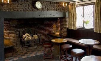 a cozy pub with a brick fireplace , wooden chairs , and a clock on the wall at The Brocket Arms