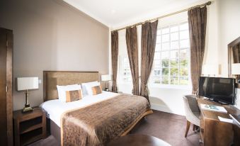 a hotel room with a large bed , two nightstands , and a window , all decorated in white and brown colors at Columba Hotel Inverness by Compass Hospitality