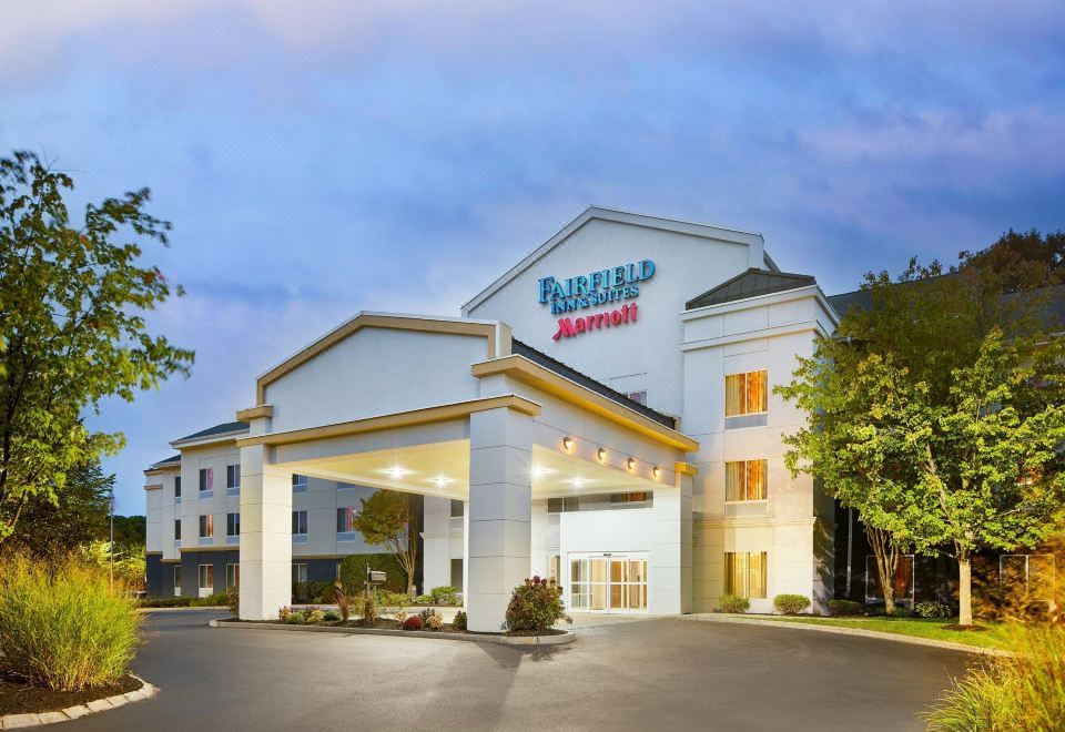a fairfield inn & suites hotel with its entrance illuminated , surrounded by trees and a parking lot at Fairfield Inn & Suites Worcester Auburn