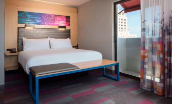 a modern hotel room with a large bed , a blue bench , and a colorful abstract painting on the wall at Aloft Coral Gables