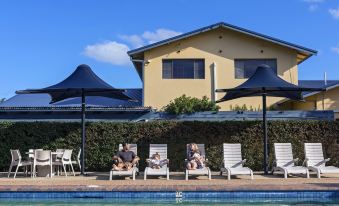 a group of people sitting on lounge chairs near a swimming pool , enjoying their time in the sun at Discovery Parks - Ballina