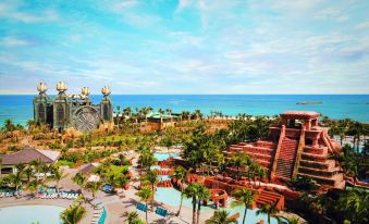 a panoramic view of a resort with a pool , water slides , and palm trees , set against the backdrop of a sunny day at The Royal at Atlantis