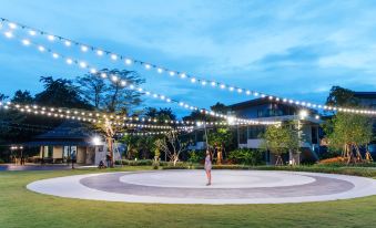 a woman is standing on a circular platform in an open field with string lights at Na Tree Tara Riverside Resort Amphawa Damnoensaduak