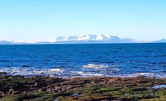 a rocky shoreline with snow - capped mountains in the background , under a clear blue sky at The Anchorage Hotel