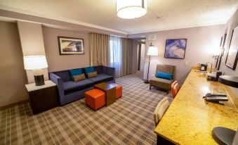 a modern hotel room with a large window , blue couch , wooden coffee table , and orange and blue ottomans at Embassy Suites by Hilton Kansas City Overland Park