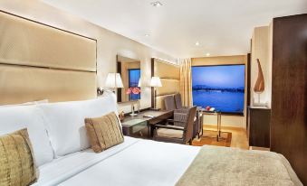 a large bed with white linens is in a room with a desk , chair , and window at The Oberoi Zahra, Luxury Nile Cruiser