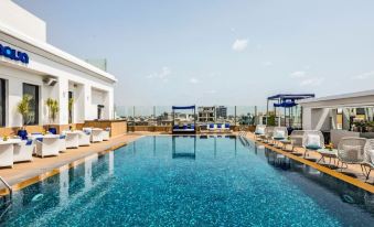 a large outdoor swimming pool surrounded by lounge chairs and umbrellas , with a view of the city skyline in the background at The Park Chennai