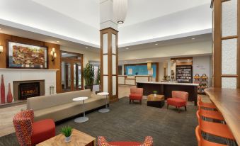 a modern hotel lobby with various seating options , including couches and chairs , as well as a reception desk at Hilton Garden Inn Stony Brook