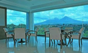 a room with white chairs and tables in front of a large window , offering a view of a mountain and trees at Braja Mustika Hotel Bogor