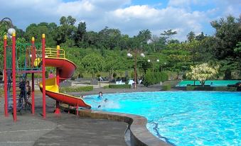 a large swimming pool with a red slide and yellow slide in the background , surrounded by trees at Braja Mustika Hotel Bogor