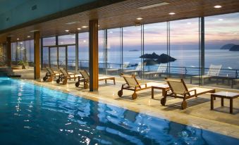 an indoor swimming pool surrounded by chairs and a view of the ocean through large windows at Hotel Dubrovnik Palace