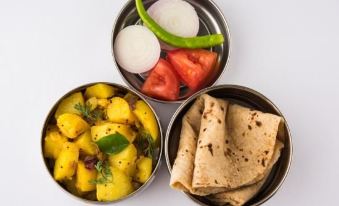 three metal containers filled with different types of food , including potatoes , onions , and tomatoes , and a slice of pita bread at Collection O 27949 Hotel Kriti Green