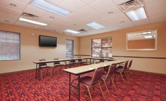a conference room with rows of tables and chairs , a television mounted on the wall , and large windows at Residence Inn West Springfield