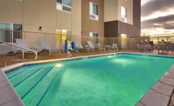 an outdoor pool surrounded by a hotel , with several people enjoying their time in the pool at TownePlace Suites Clovis
