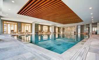 an indoor swimming pool with a wooden ceiling , surrounded by windows and marble floors , creating a spa - like atmosphere at Sheraton Grand Samsun Hotel