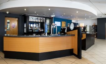 a modern , curved bar area with wooden countertops and multiple wine bottles on display , along with blue walls and white tiled floor at Holiday Inn Express Newcastle Gateshead