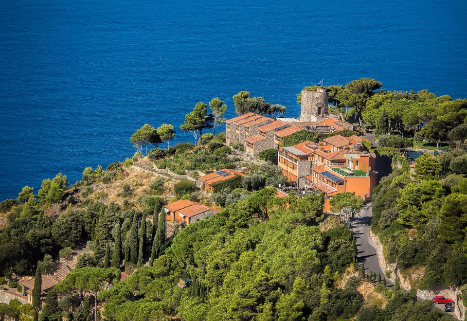 aerial view of a red brick house surrounded by trees and overlooking a body of water at Boutique Hotel Torre di Cala Piccola