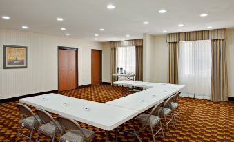 a large , empty conference room with multiple white tables and chairs , wooden doors , and a carpeted floor at Holiday Inn Express & Suites Jackson