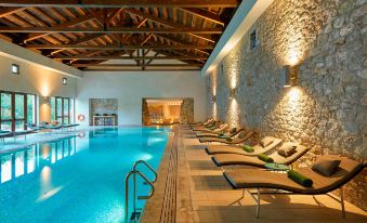 a large indoor swimming pool with stone walls and wooden floors , surrounded by lounge chairs at The Romanos, a Luxury Collection Resort, Costa Navarino
