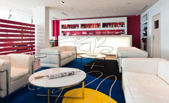 a modern lounge area with white furniture , blue and yellow carpet , and a bar in the background at Hotel Victoria