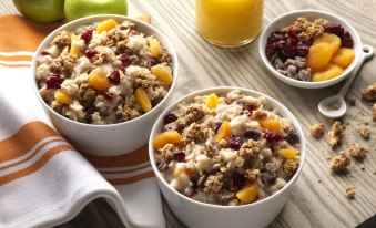two bowls of granola with fruit and nuts are placed on a table next to a glass of orange juice at Home2 Suites by Hilton Canton