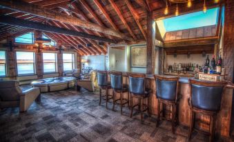 a cozy wooden bar with multiple stools and chairs , surrounded by windows that offer a view of the ocean at The Cannery Lodge