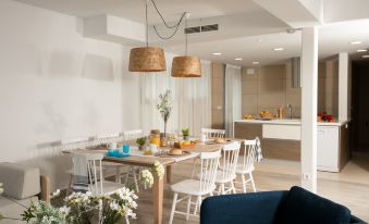 a dining room with a table surrounded by white chairs , and a kitchen visible in the background at Pierre & Vacances Blanes Playa