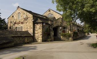 a stone building with a sign on the front , located in a village setting near a river at Huddersfield North